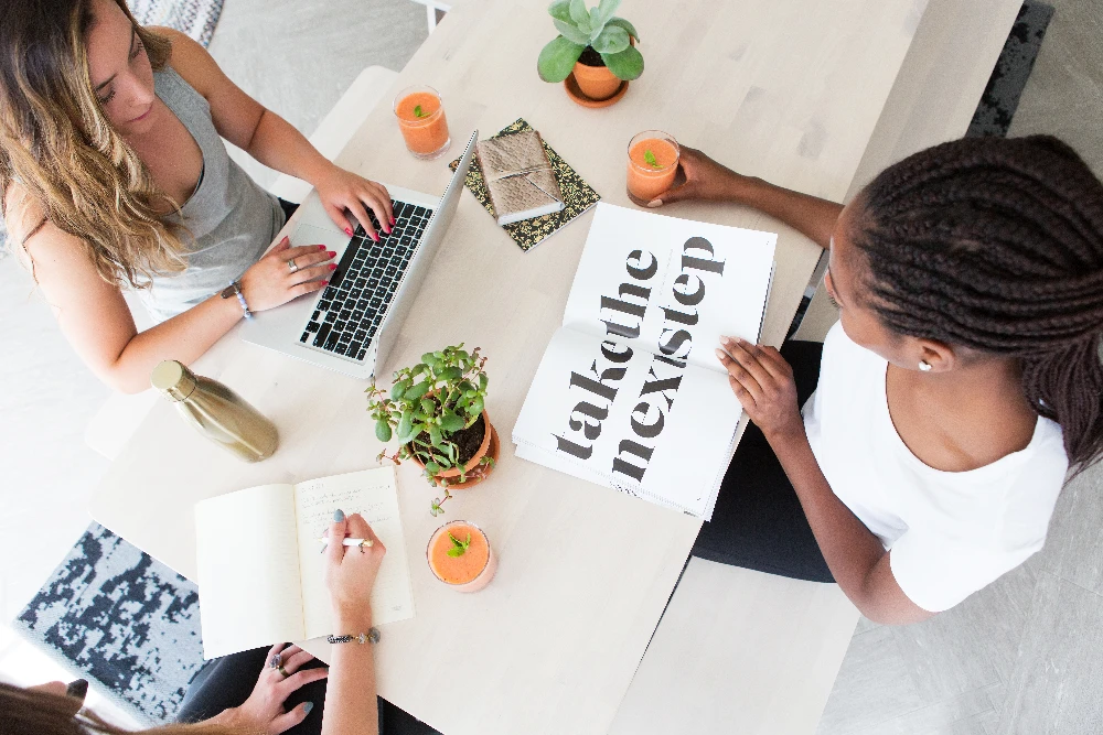 promotional image for marketing services provided by CSRA Marketing, a local service business website & amrketing agency. Image shows: people sitting at a table, notebook open to a section that reads: Take the next step